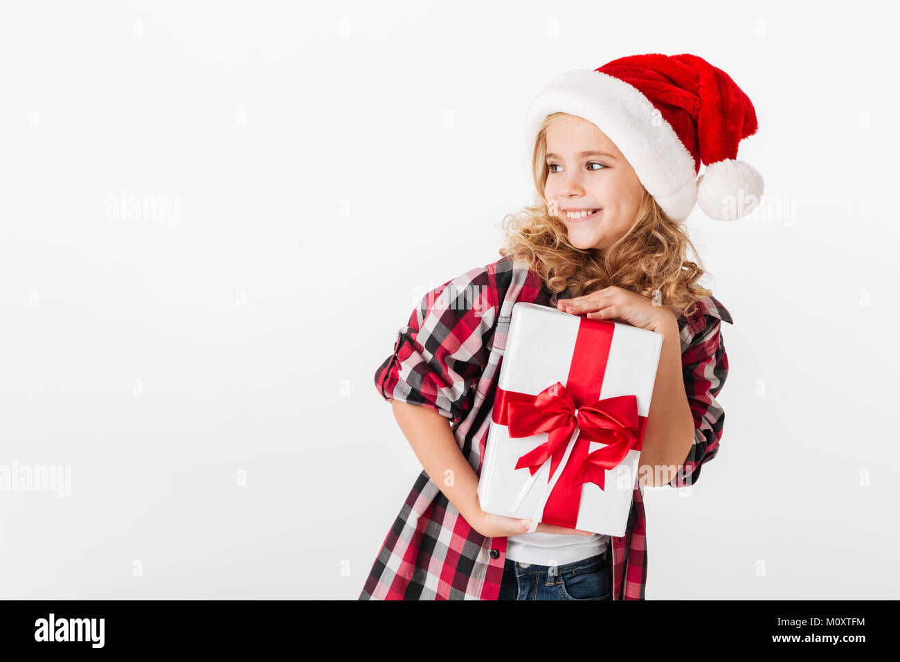 Portrait of a cheery little girl holding gift box and looking away at ...
