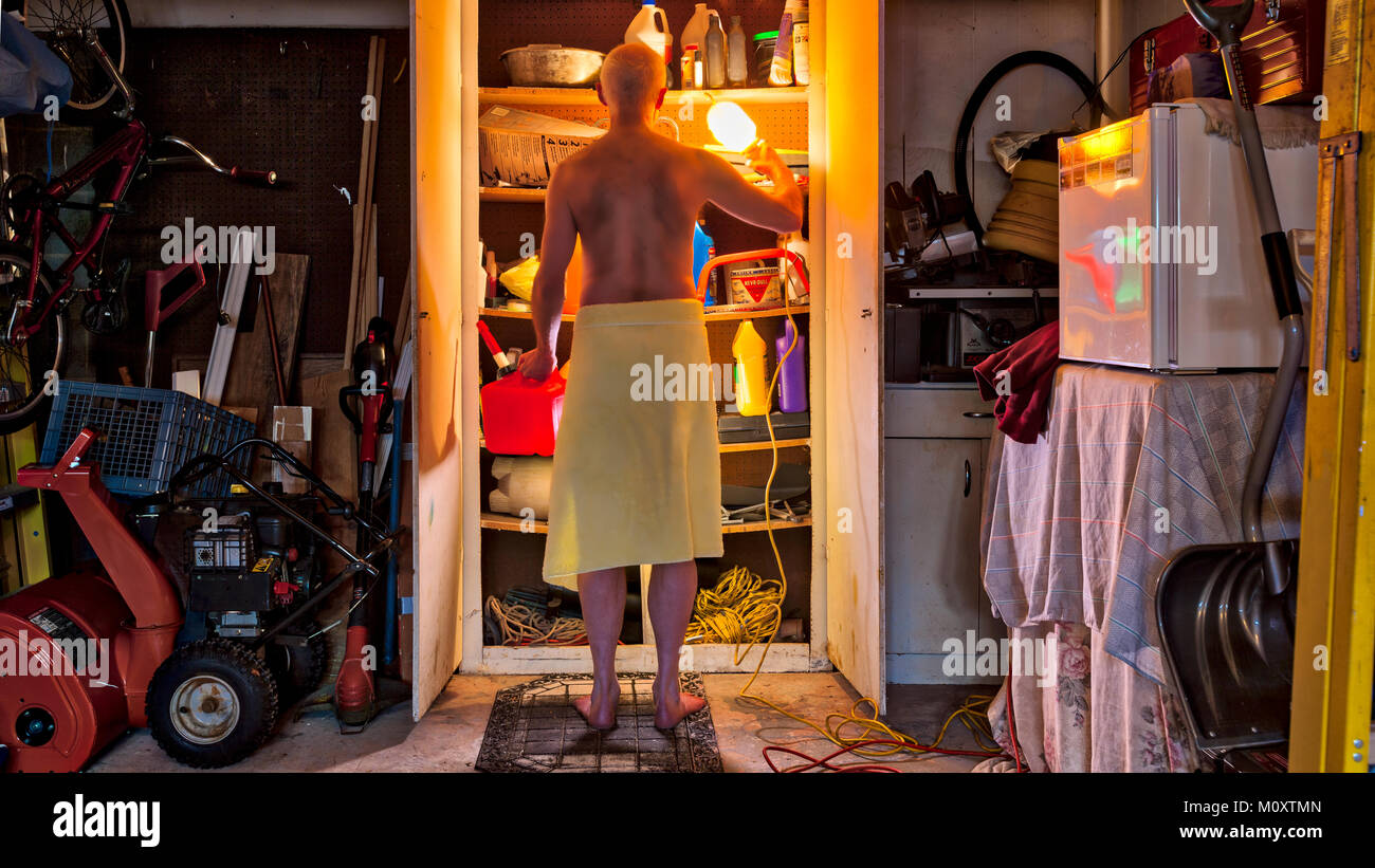 A bachelor man wearing only a towel, in the garage searching for something in a closet. Stock Photo