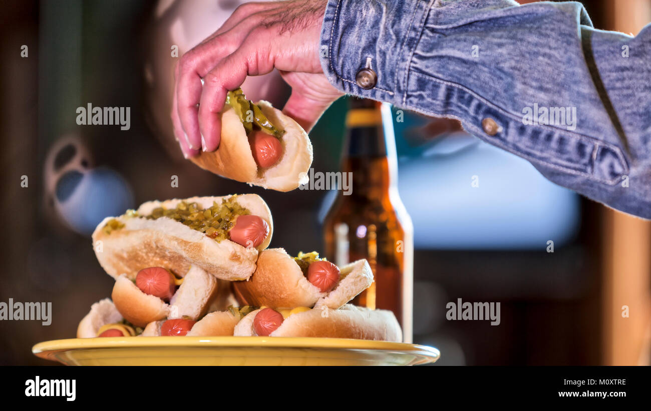 A bachelor man watching TV and eating hot dogs. Stock Photo