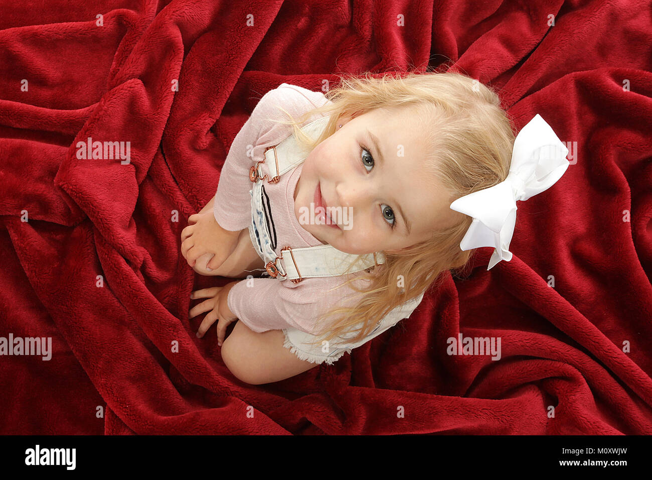 pretty 3 year old girl playing on soft red blanket Stock Photo