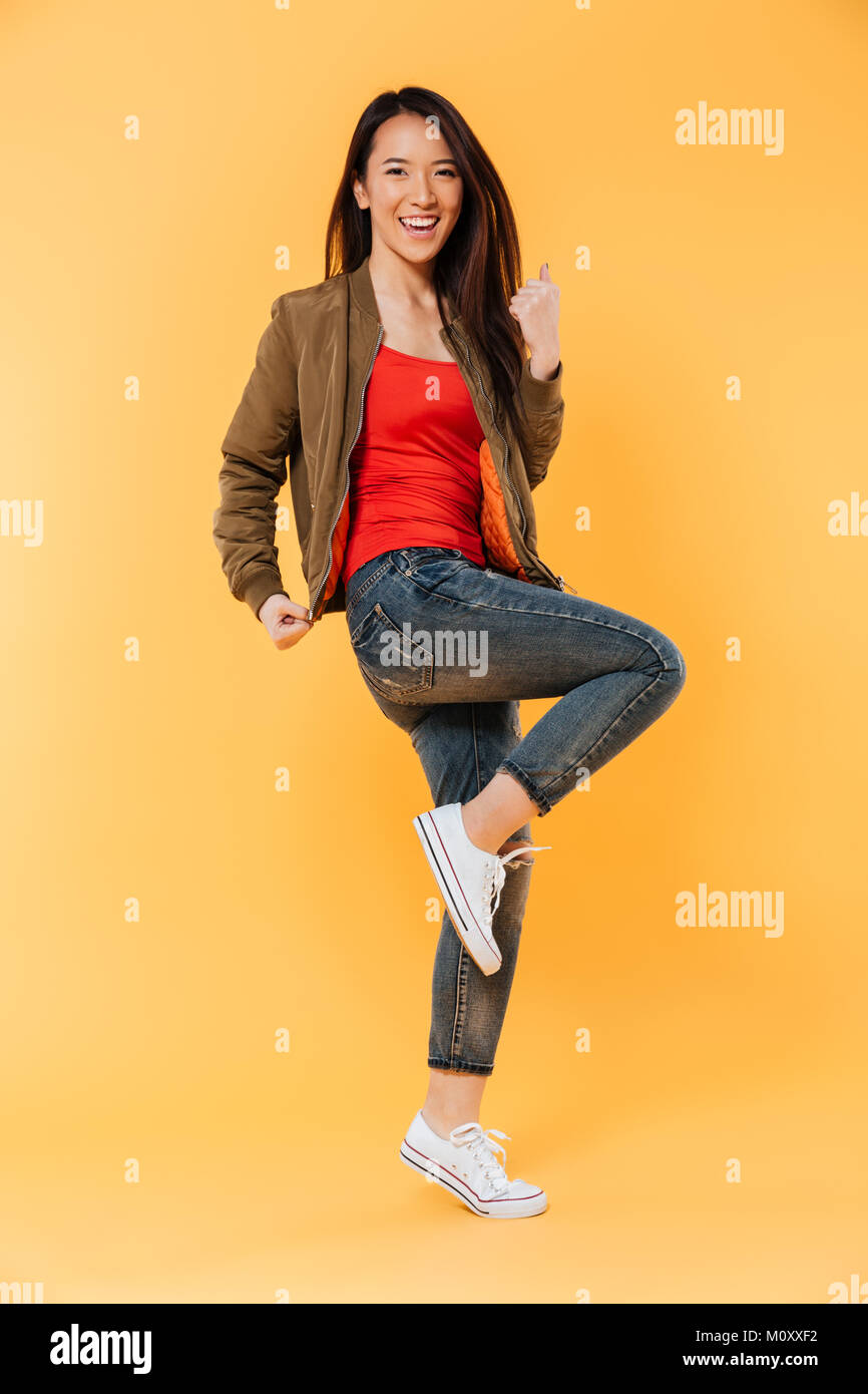 Full length portrait of a cheerful asian girl standing and celebrating ...