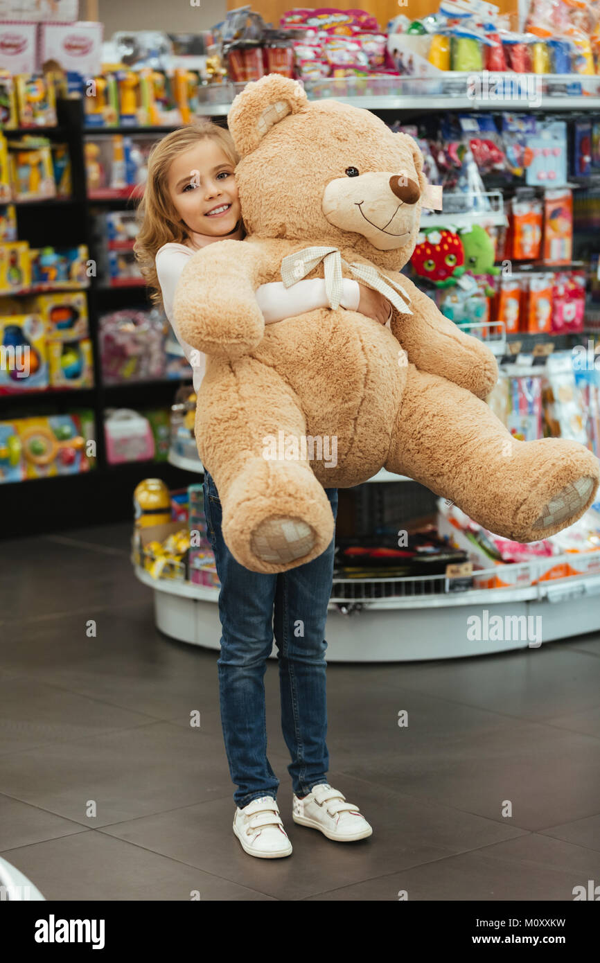 Happy little girl holding big teddy bear while standing at the ...