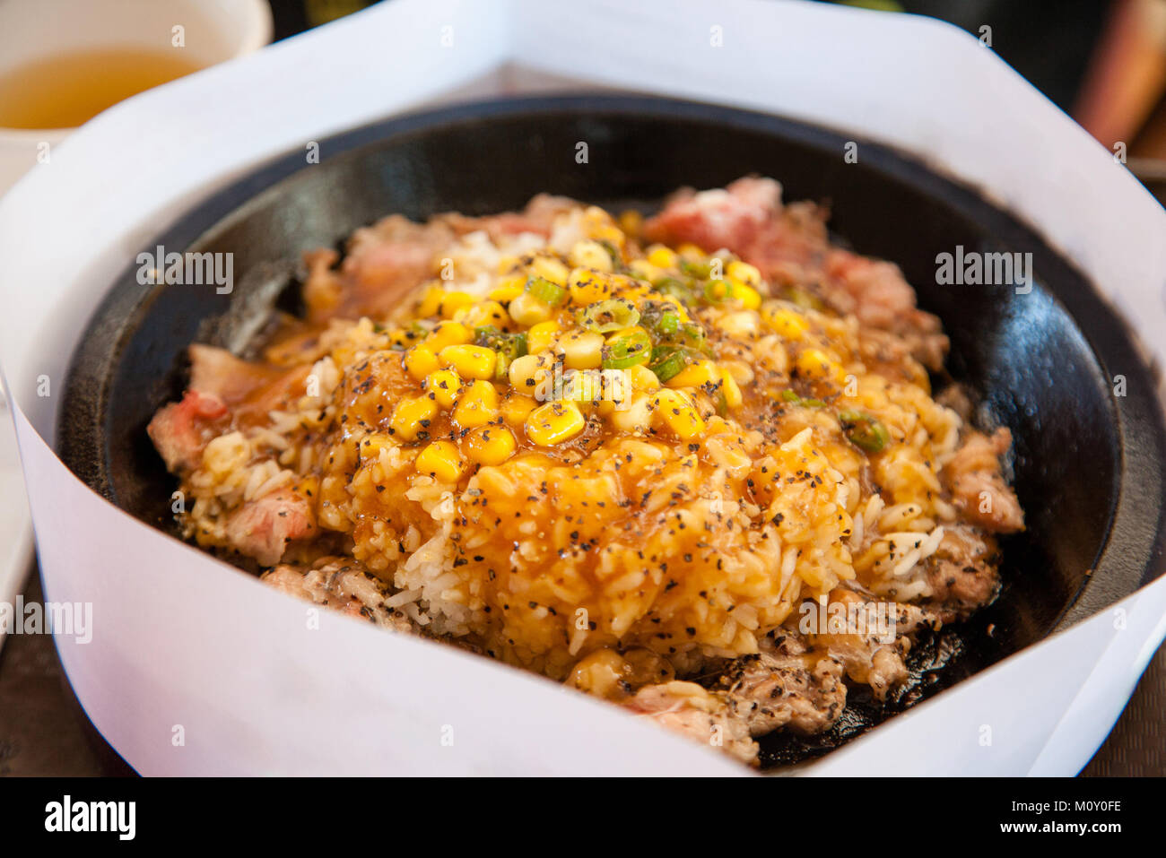 Sizzling Teppanyaki pepper steak lunch with rice topped with sweet corn and scallions on electromagnetic iron hot plate. A white piece of paper surrou Stock Photo