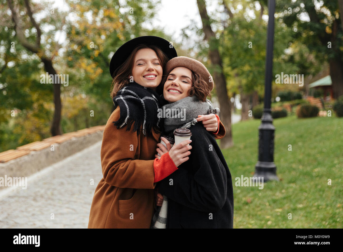 Portrait of two smiling girls dressed in autumn clothes hugging while ...