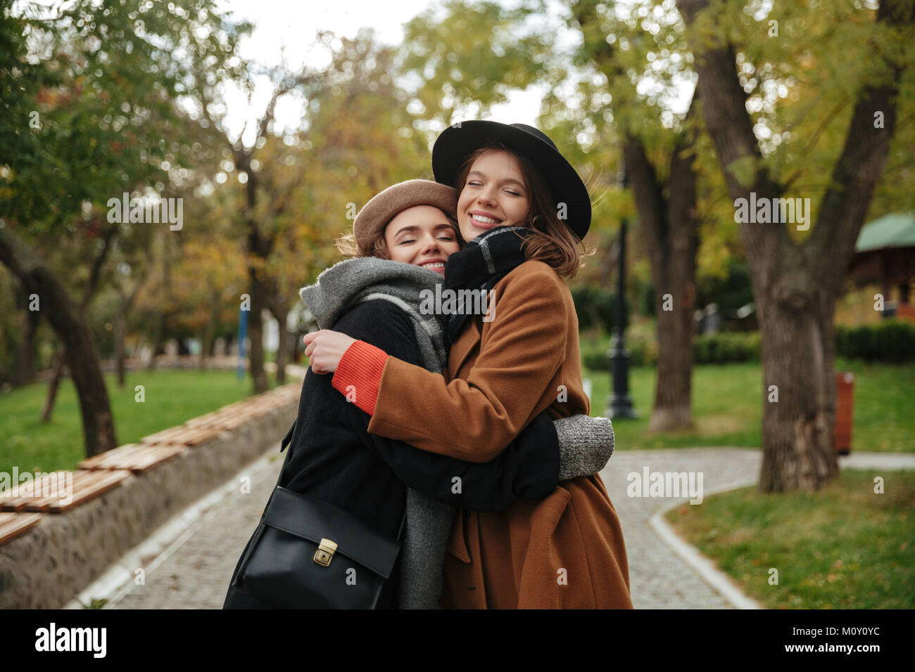 Portrait of two smiling girls dressed in autumn clothes hugging while ...