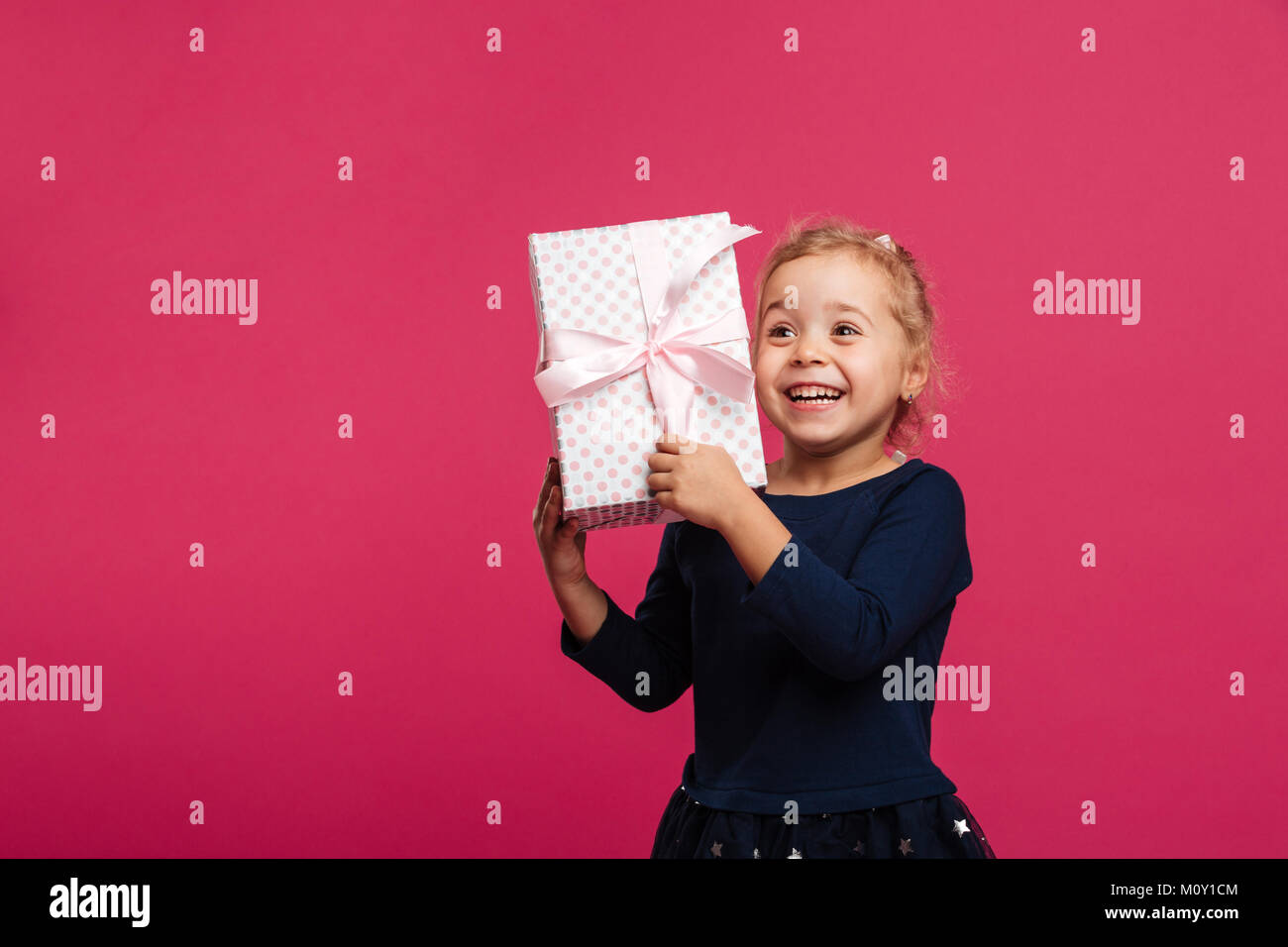 Happy young blonde girl holding gift box and rejoices while looking ...