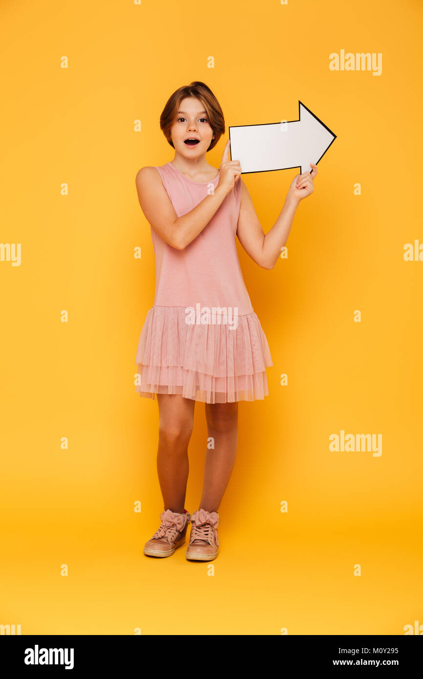 Cheerful handsome girl in pink dress holding arrow right and looking ...