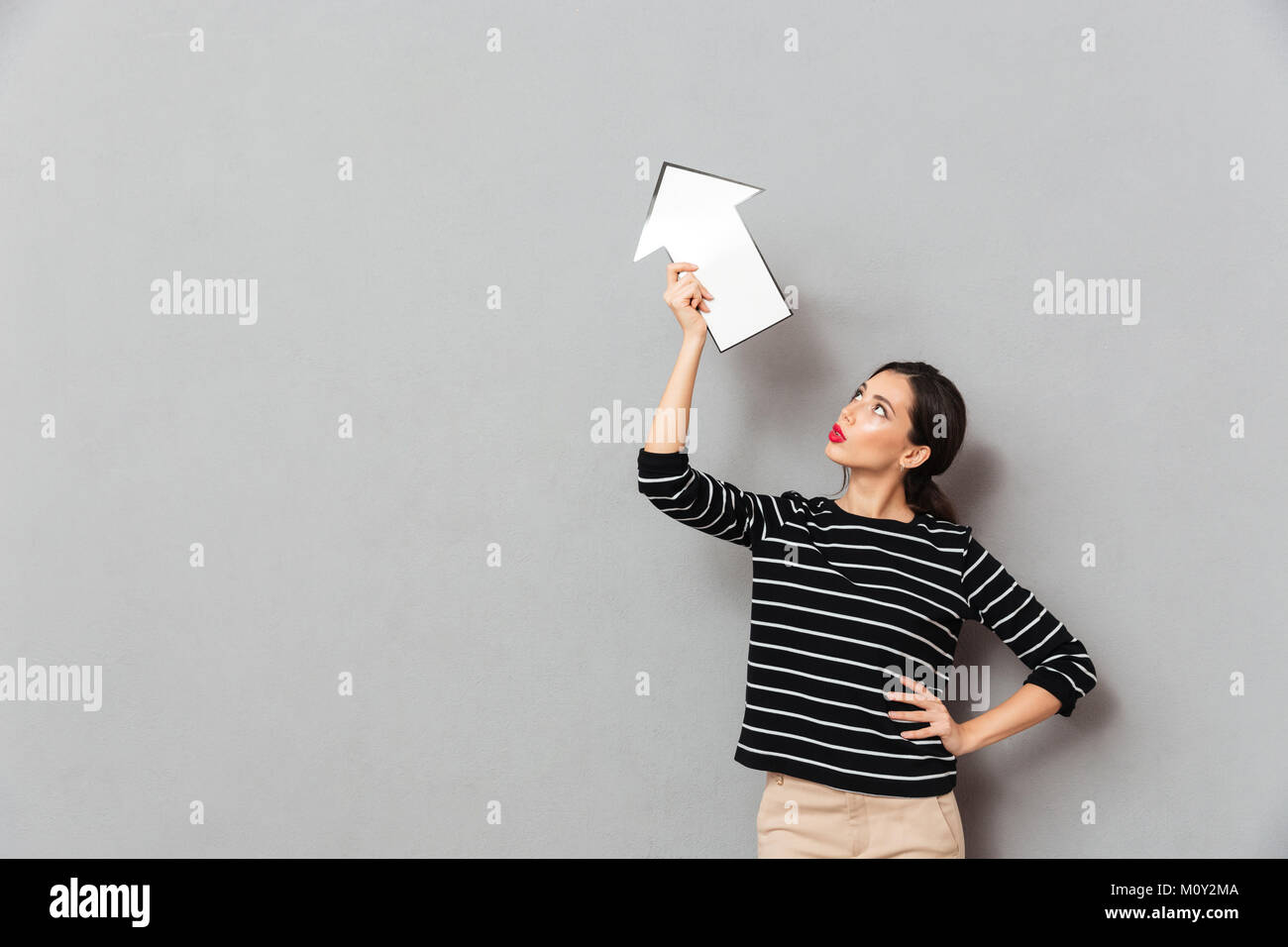 Portrait of a beautiful woman pointing up with an arrow while standing ...