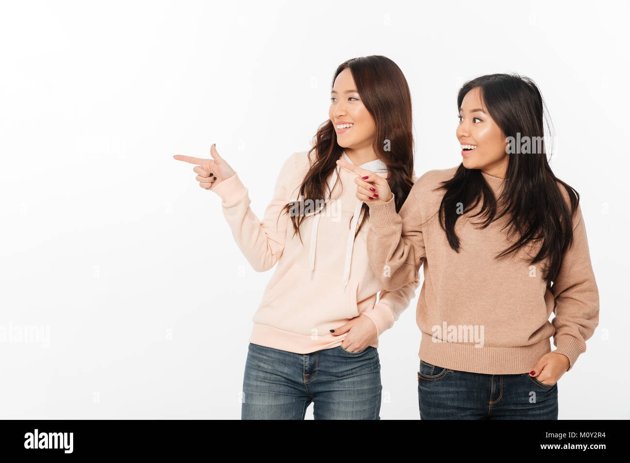 Image of two asian pretty happy ladies sisters. Looking aside pointing. Stock Photo