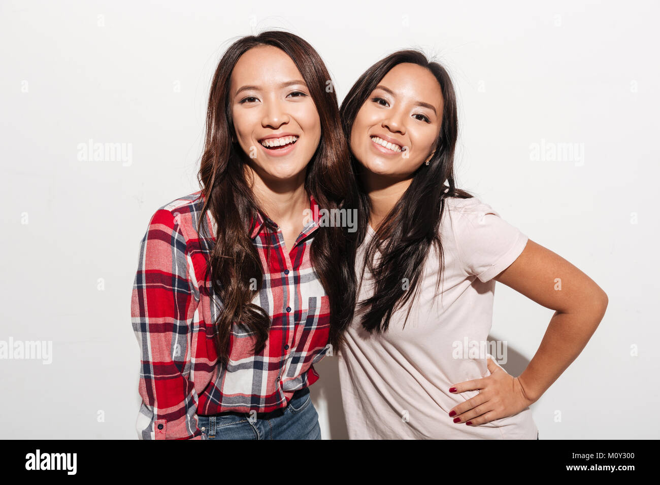 Image of two asian pretty cheerful ladies sisters hugging with each other. Looking camera. Stock Photo