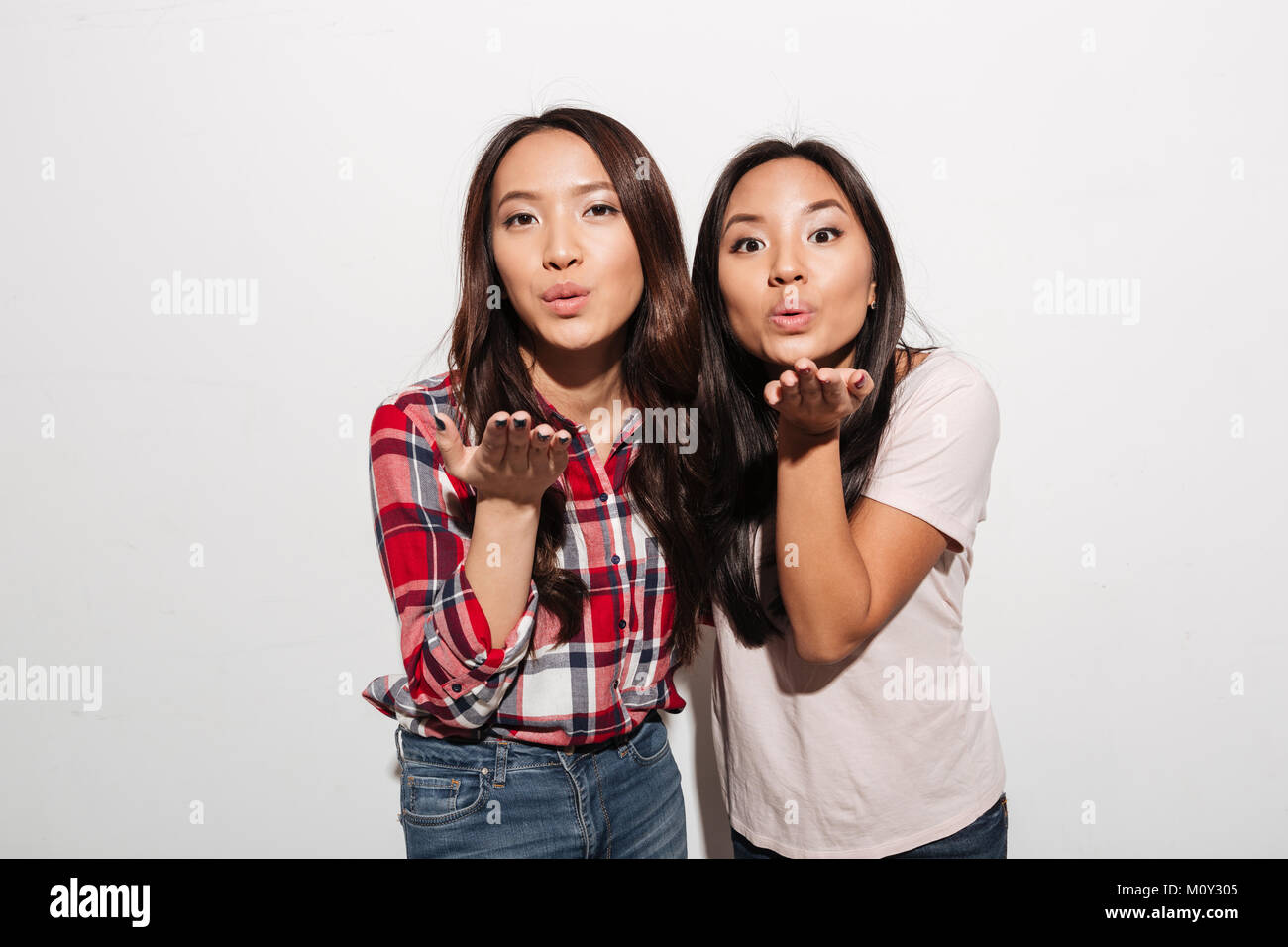 Image of two asian pretty ladies sisters. Looking camera blowing kisses. Stock Photo