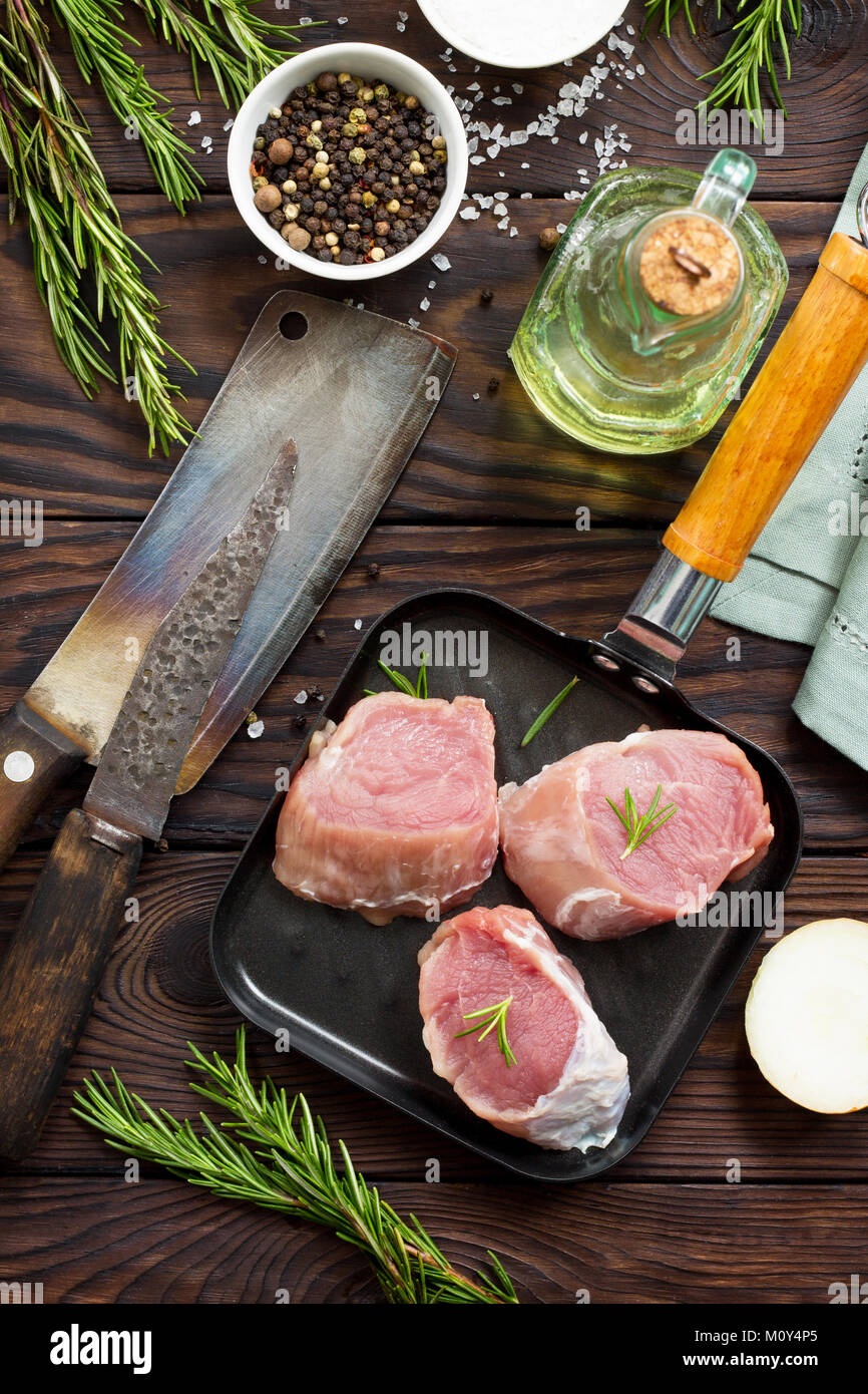 Fresh meat. Raw pork steak on a cast iron frying pan, spices and fresh rosemary on a kitchen wooden table. Stock Photo