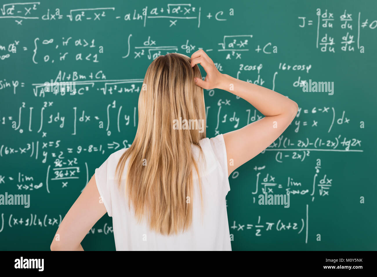 Rear View Of A Confused Girl Looking At Blackboard With Formulas In Classroom Stock Photo