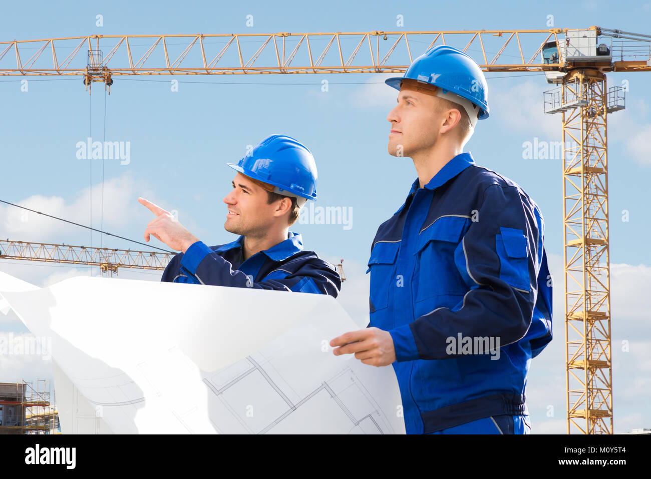 Two Young Male Architect Looking Into Blueprints At Construction Site Stock Photo