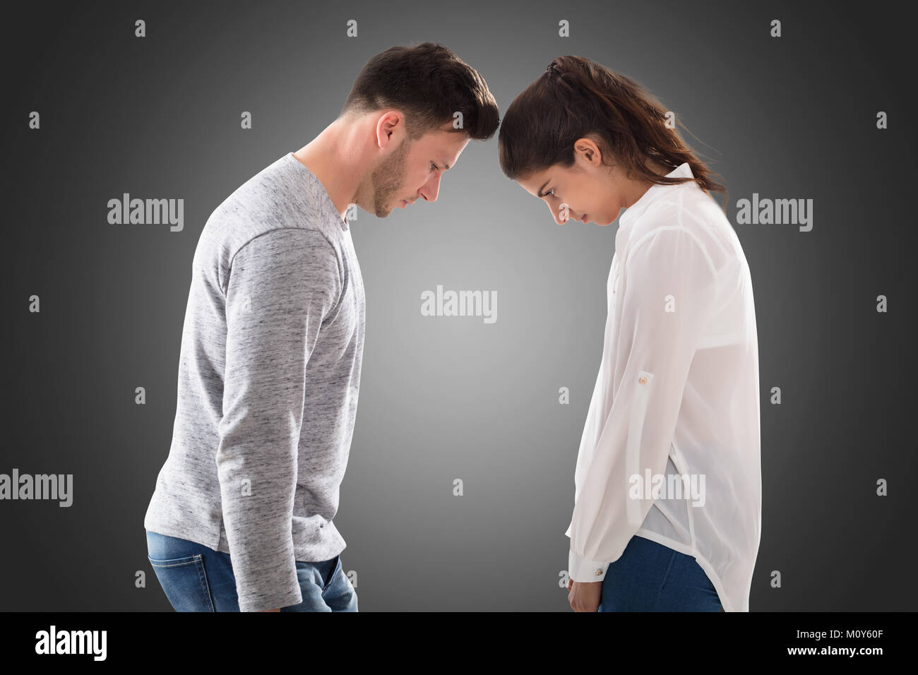 Young Sad Couple Standing Face To Face On Gray Background Stock Photo