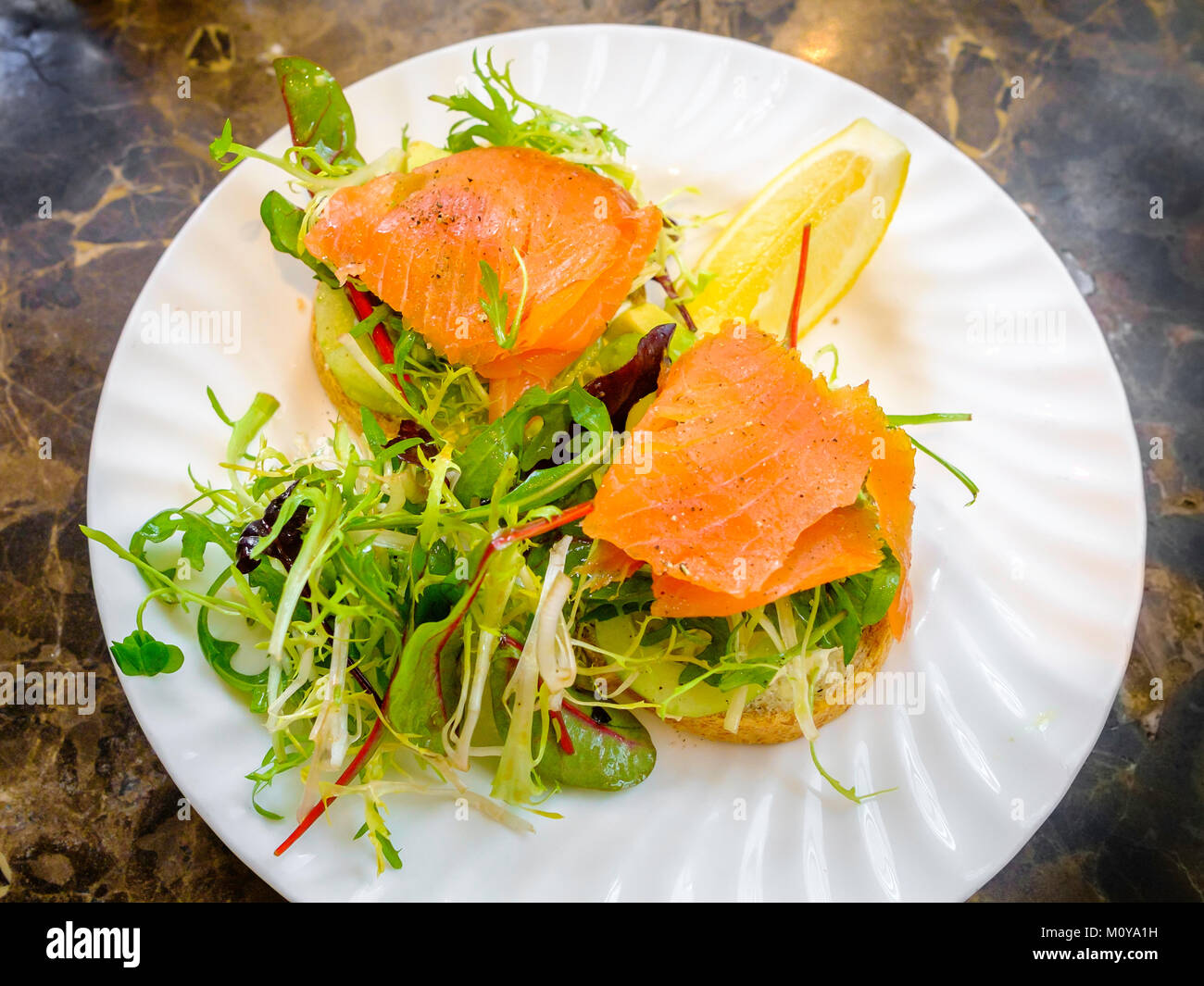 Smoked Salmon and Avocado open sandwich on granary bread with rocket salad garnish Stock Photo