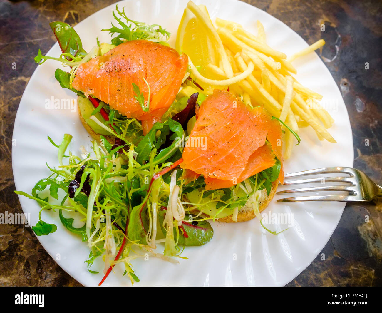 Smoked Salmon and Avocado open sandwich on granary bread with rocket salad garnish and Alumette Potatoes Stock Photo