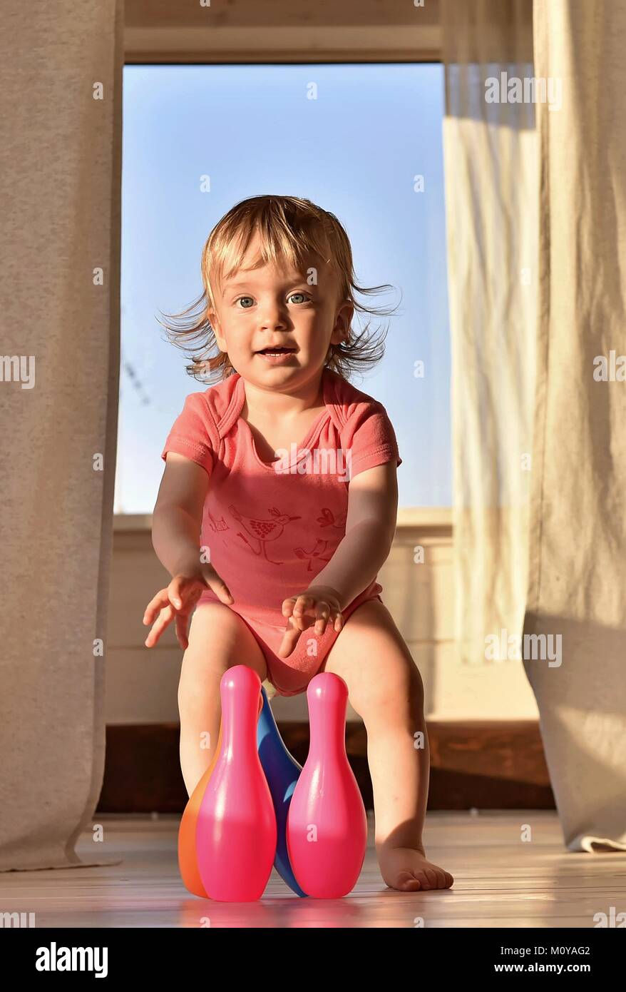 Happy smiling little girl playing bowling with colored pins. In room