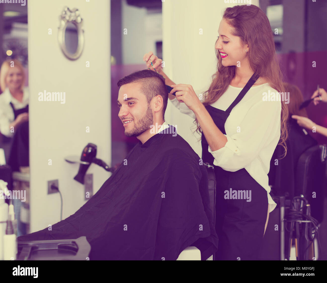 Smiling female hairdresser doing hairstyle for young men at salon