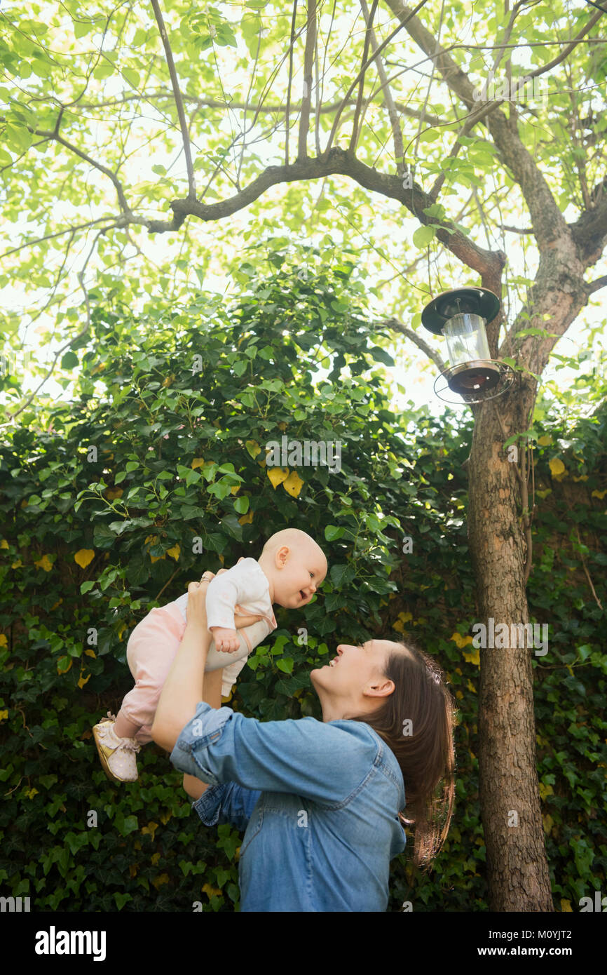 Caucasian mother lifting baby daughter under tree Stock Photo