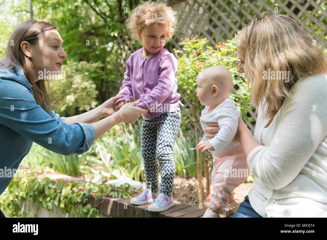 Caucasian mothers holding daughters on garden wall Stock Photo