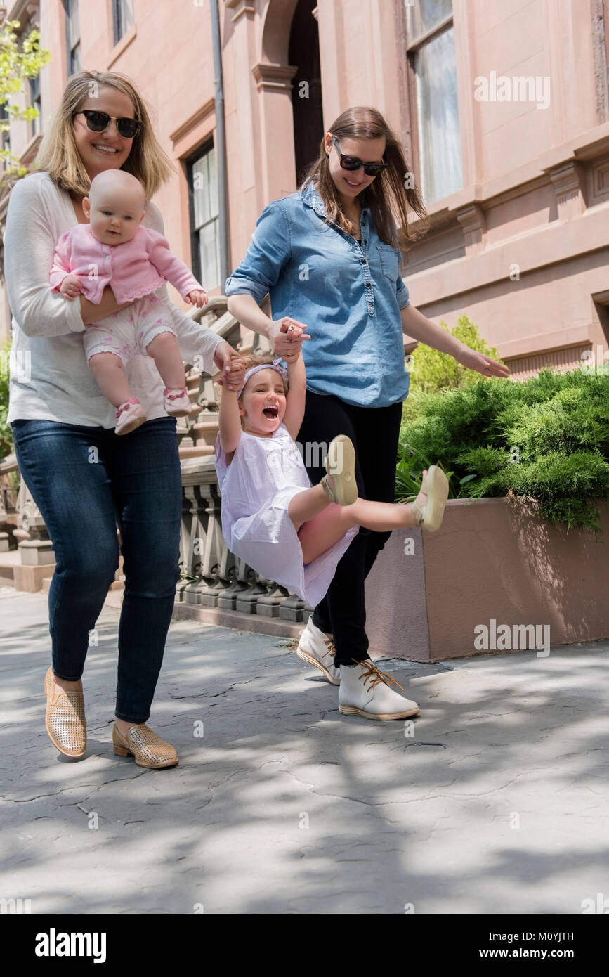 Caucasian mothers swinging daughter on city sidewalk Stock Photo