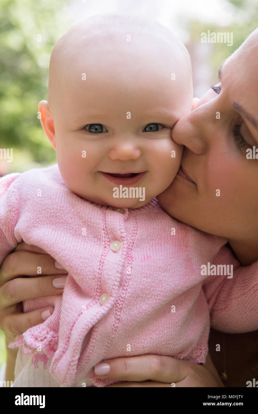 Portrait of Caucasian mother kissing cheek of baby daughter Stock Photo