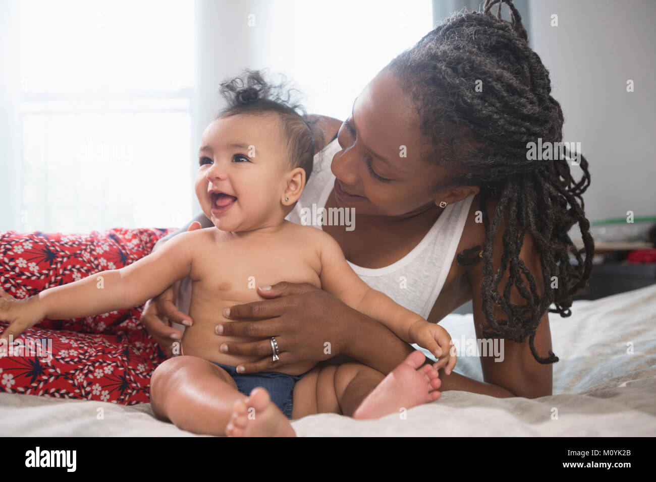Mother holding smiling baby daughter on bed Stock Photo