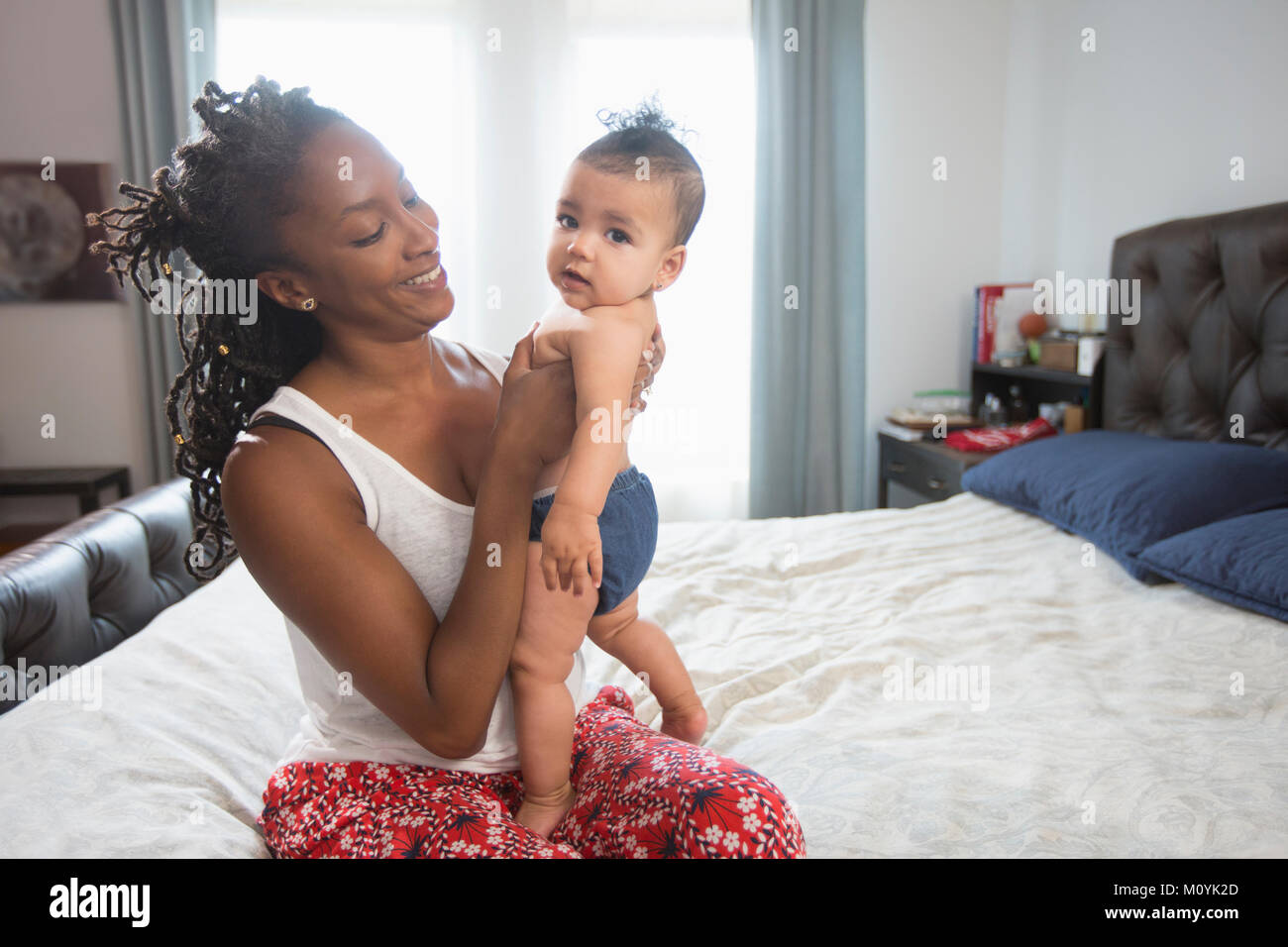 Mother sitting on bed holding baby daughter Stock Photo