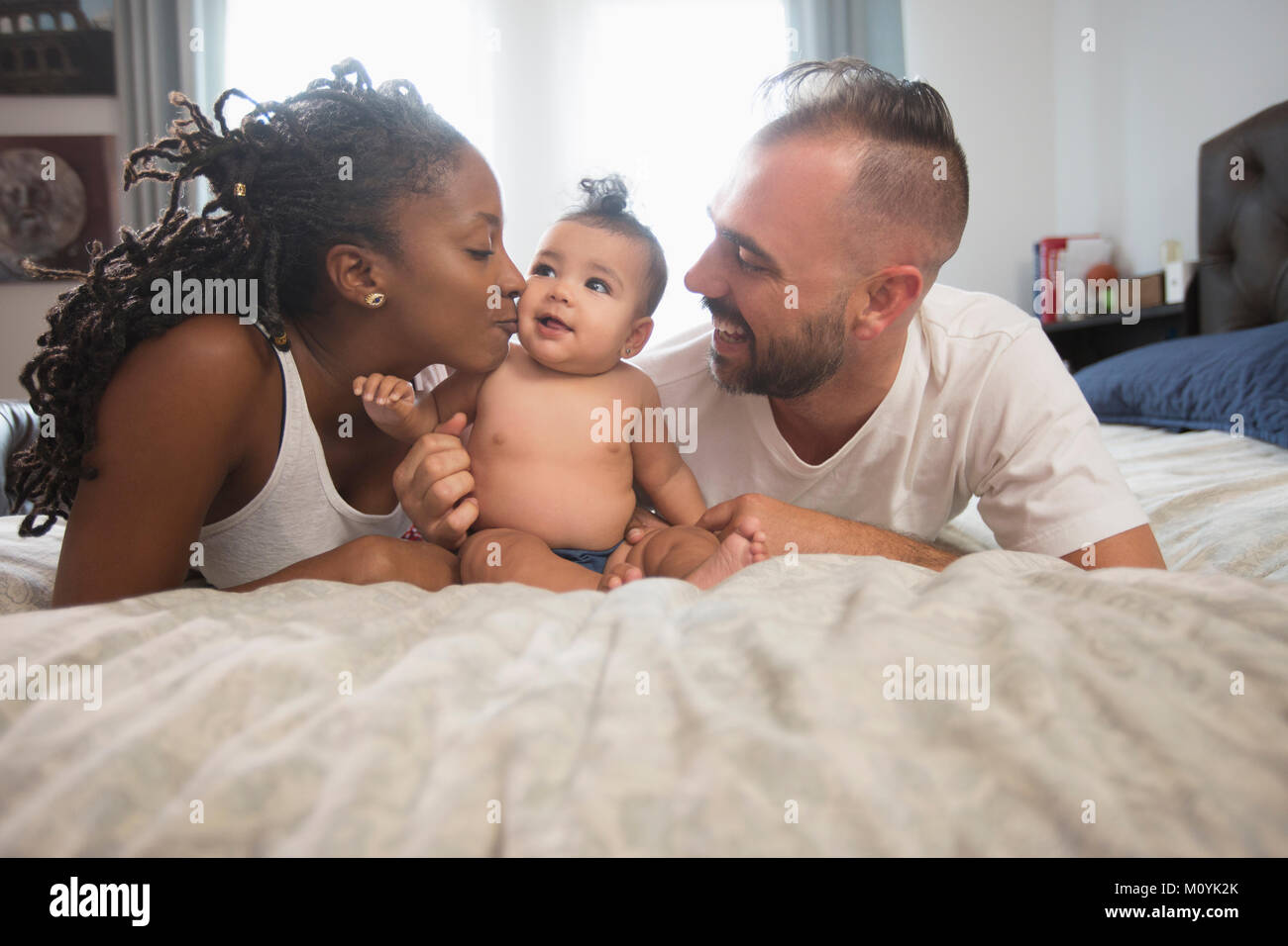 Mother and father laying on bed with baby daughter Stock Photo