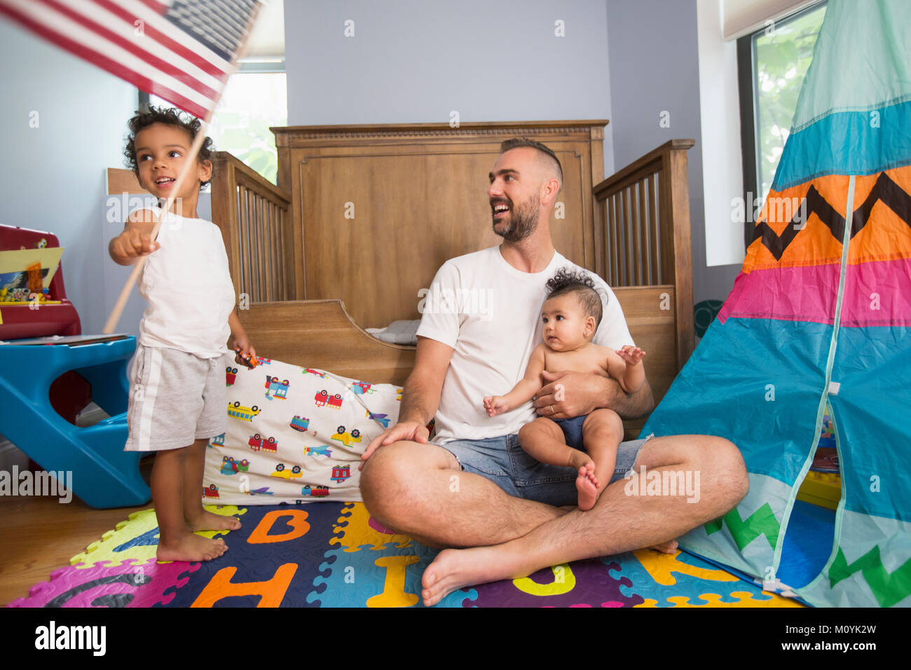 Father watching son waving American flag in playroom Stock Photo