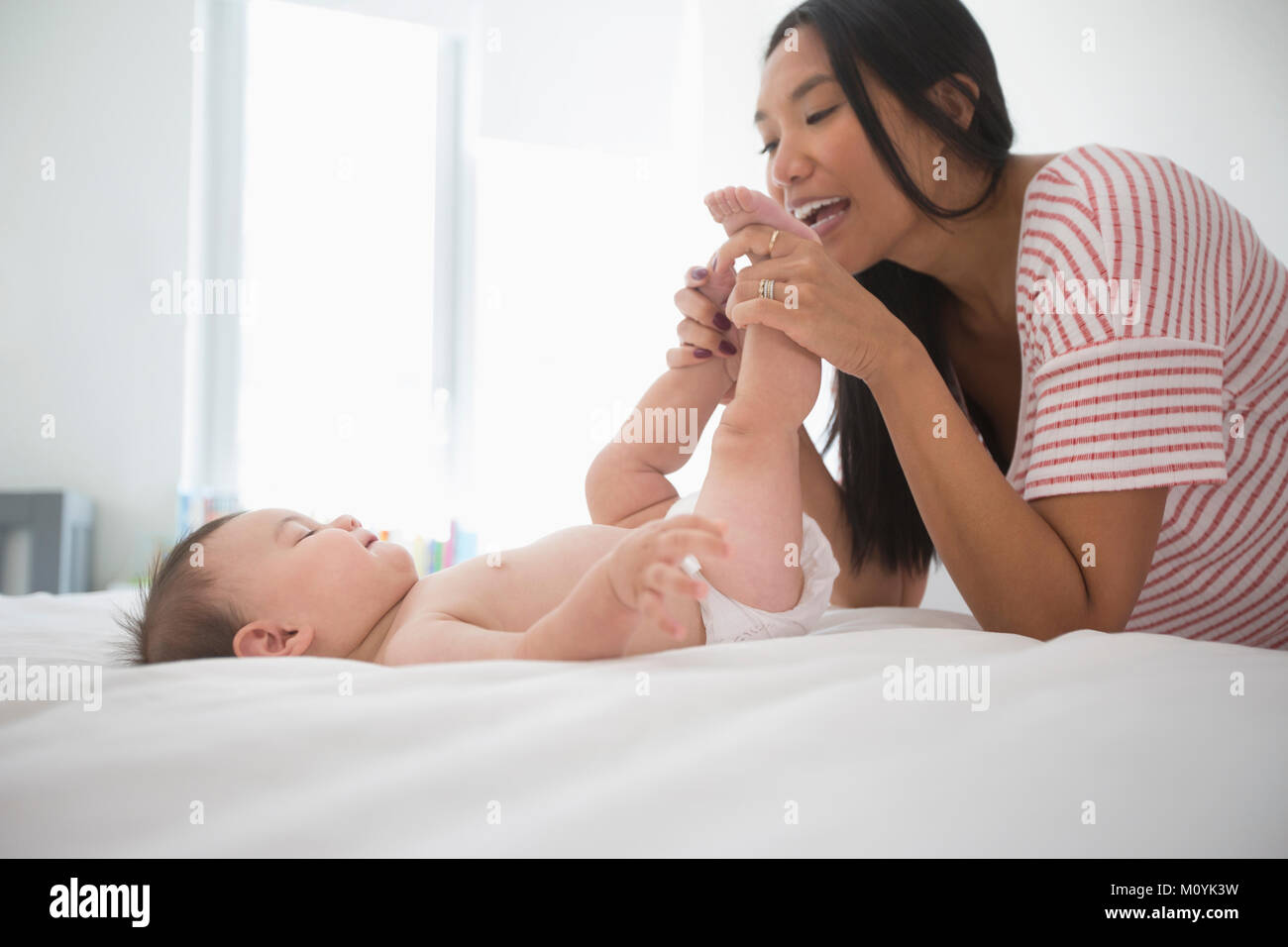 Mother playing with feet of baby son laying on bed Stock Photo