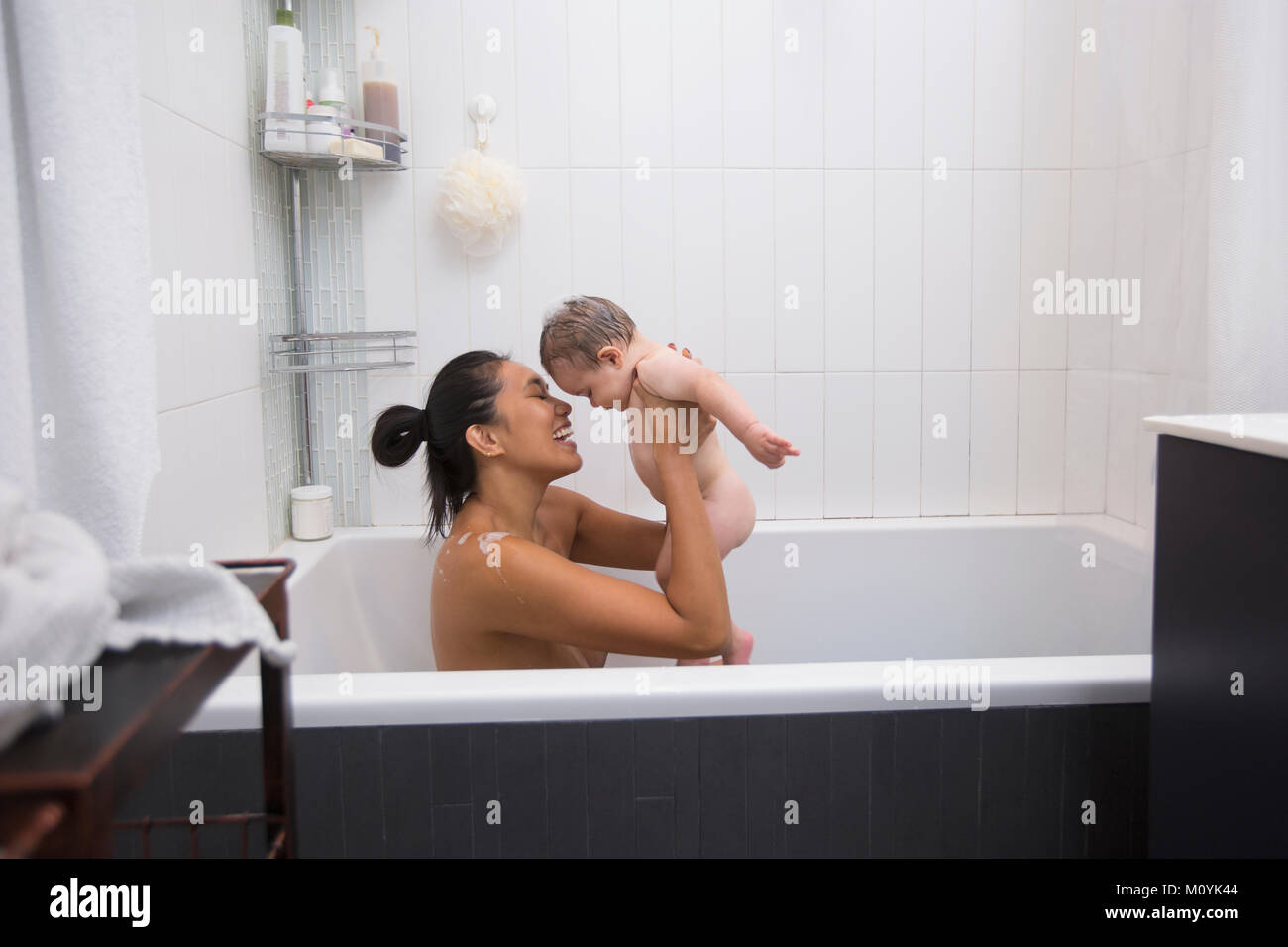 Mother sitting in bathtub holding baby son Stock Photo