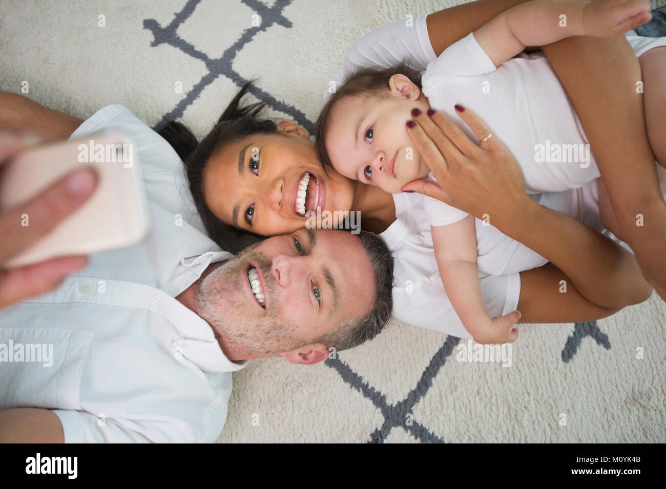 Family laying on floor posing for cell phone selfie Stock Photo