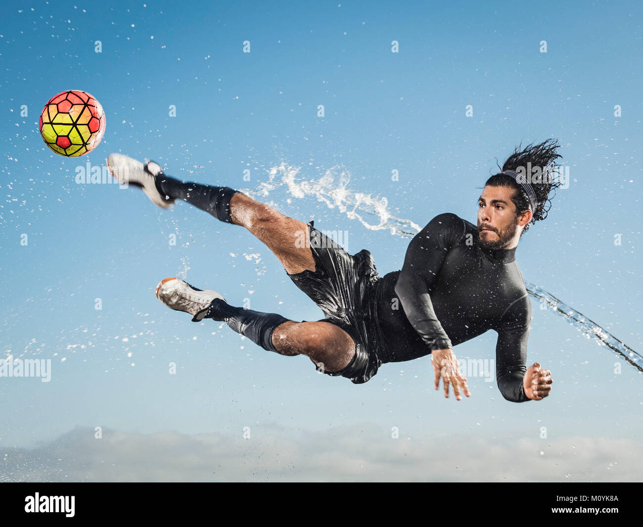 Water spraying on Hispanic man kicking soccer ball Stock Photo