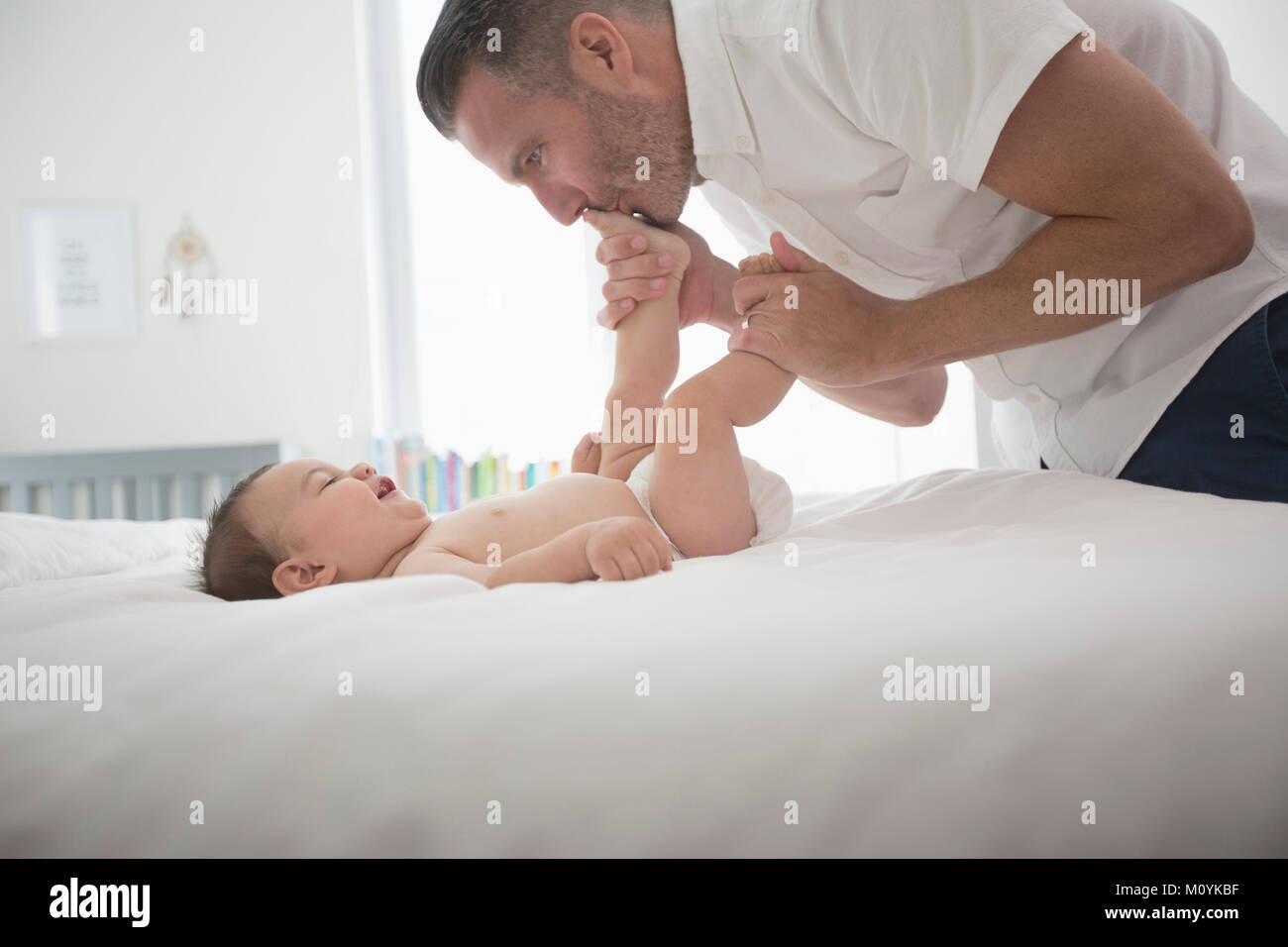 Father kissing feet of baby son on bed Stock Photo