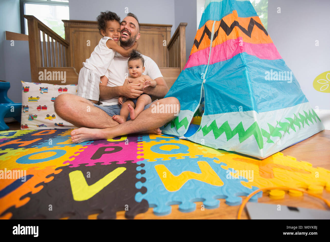 Father sitting on playroom floor holding son and daughter Stock Photo
