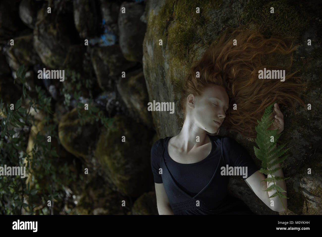 Caucasian woman with red hair laying on rock Stock Photo - Alamy