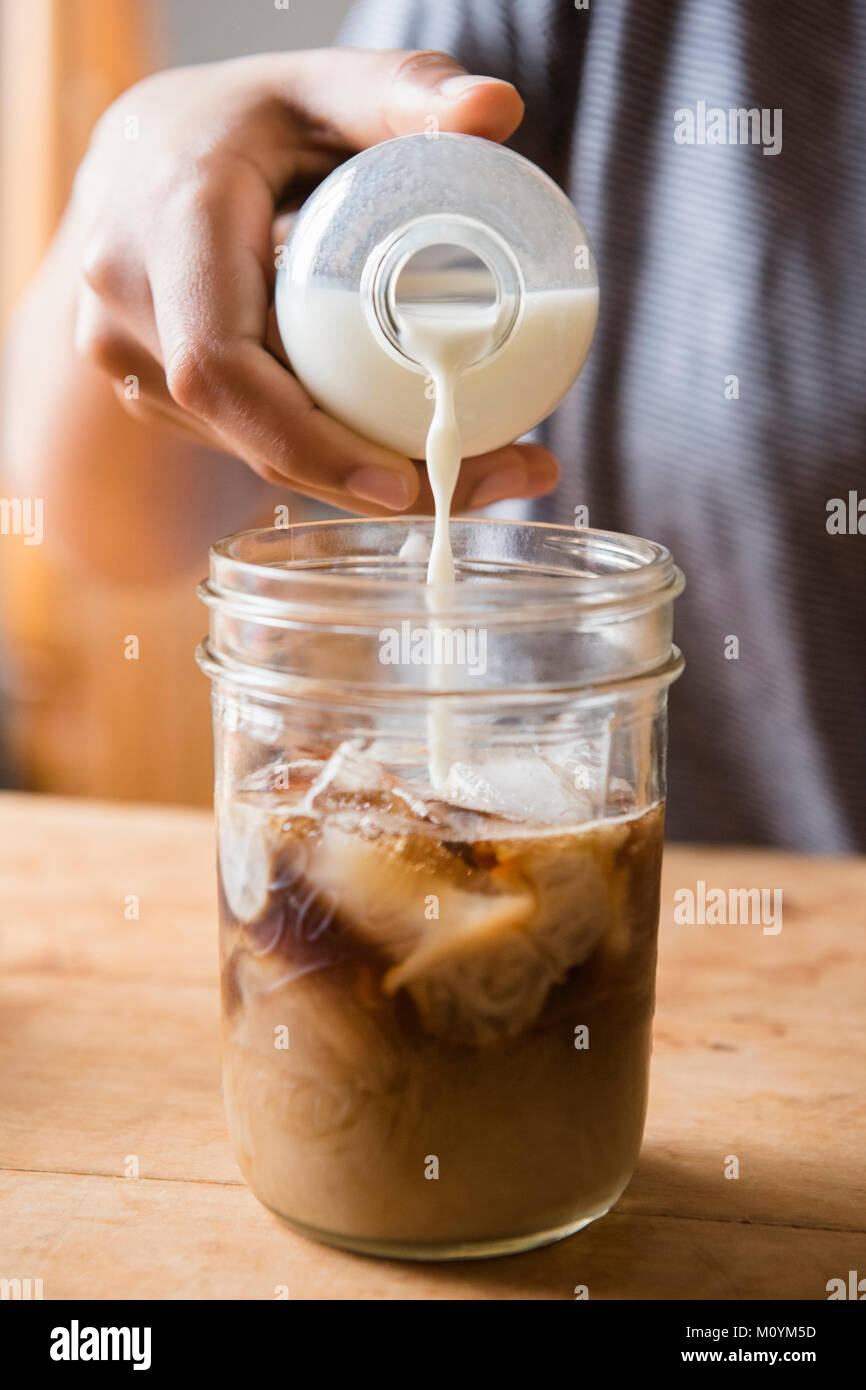 African American woman pouring milk into jar of coffee Stock Photo