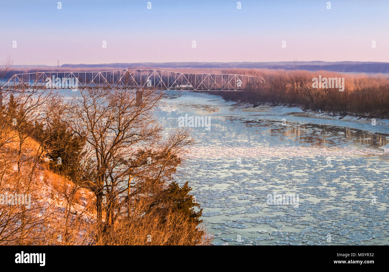 View of Missouri River at sunset in early spring; floes floating down the river; highway bridge in the background; steep shore on the left, Missouri Stock Photo