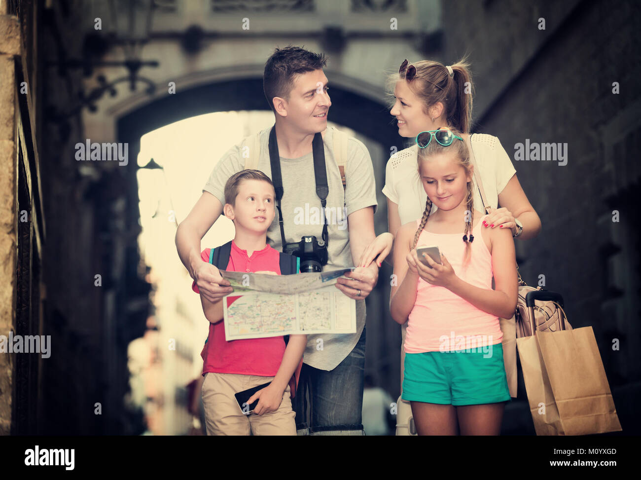 Smiling young parents with two kids traveling together using paper map ...