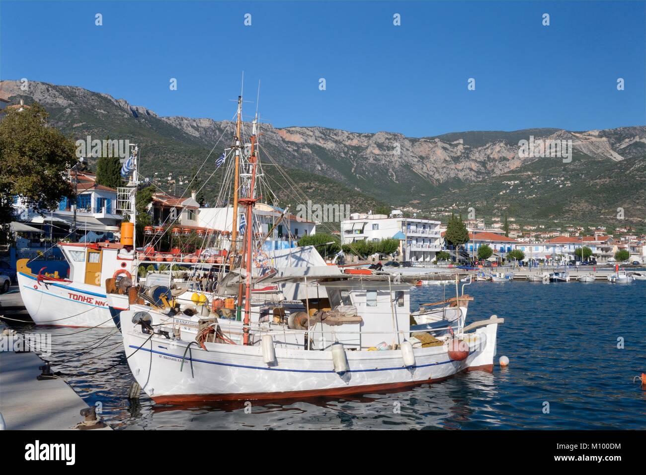 Fishing boats moored in Tyros harbour with Tyros village and mountains of Arcadia in the background, Peloponnese, Greece, August. Stock Photo