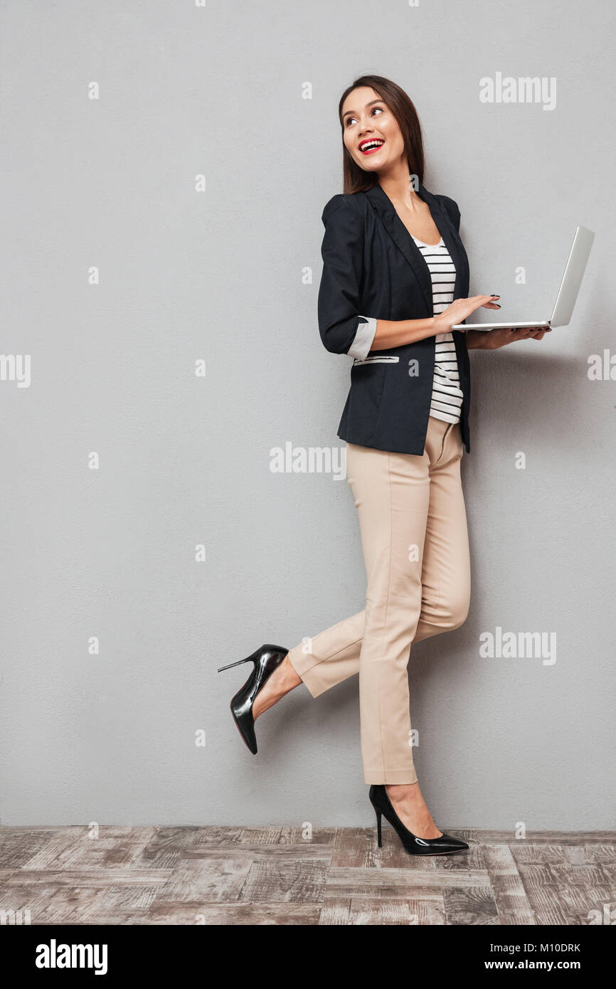 Full length image of Happy asian business woman holding laptop computer ...
