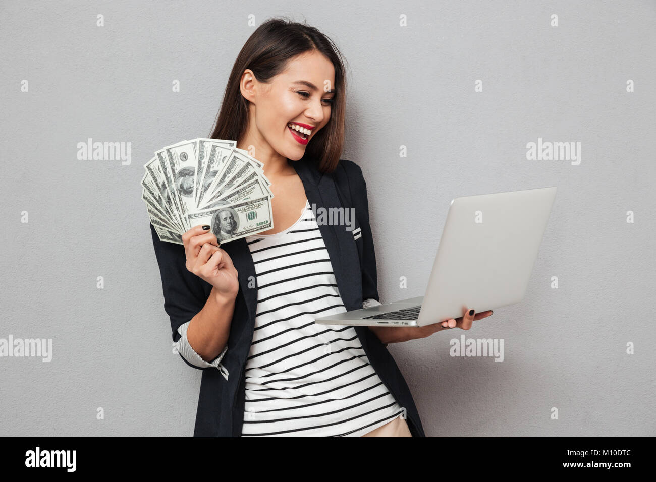 Happy Asian Business Woman Holding Money And Laptop Computer Over Gray happy-asian-business-woman-holding-money-and-laptop-computer-over-gray