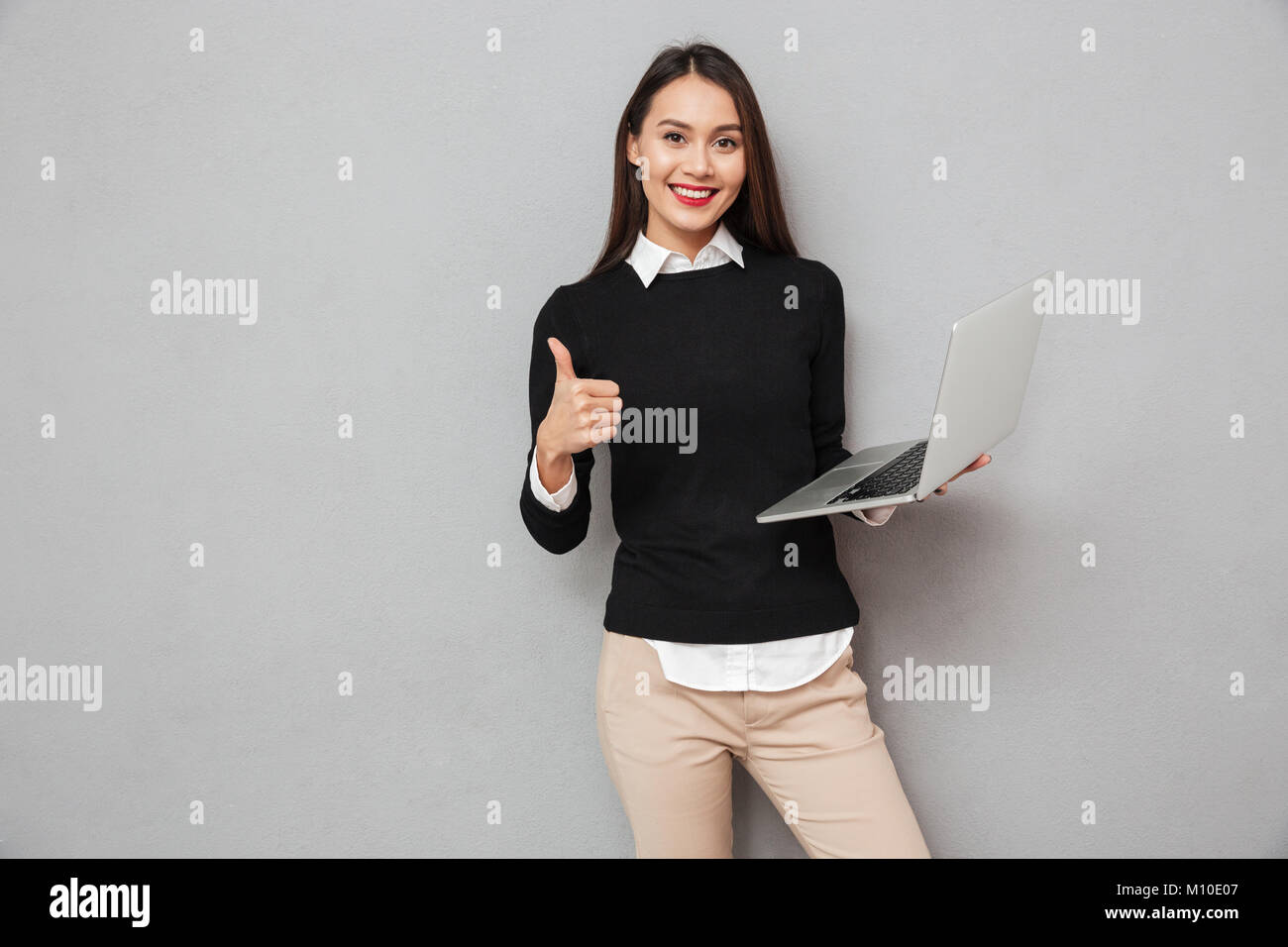 Pleased asian woman in business clothes holding laptop computer and ...