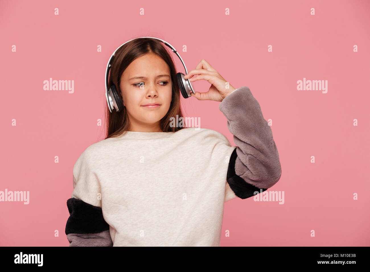 Young displeased girl push her headphones because of loudness isolated over pink Stock Photo