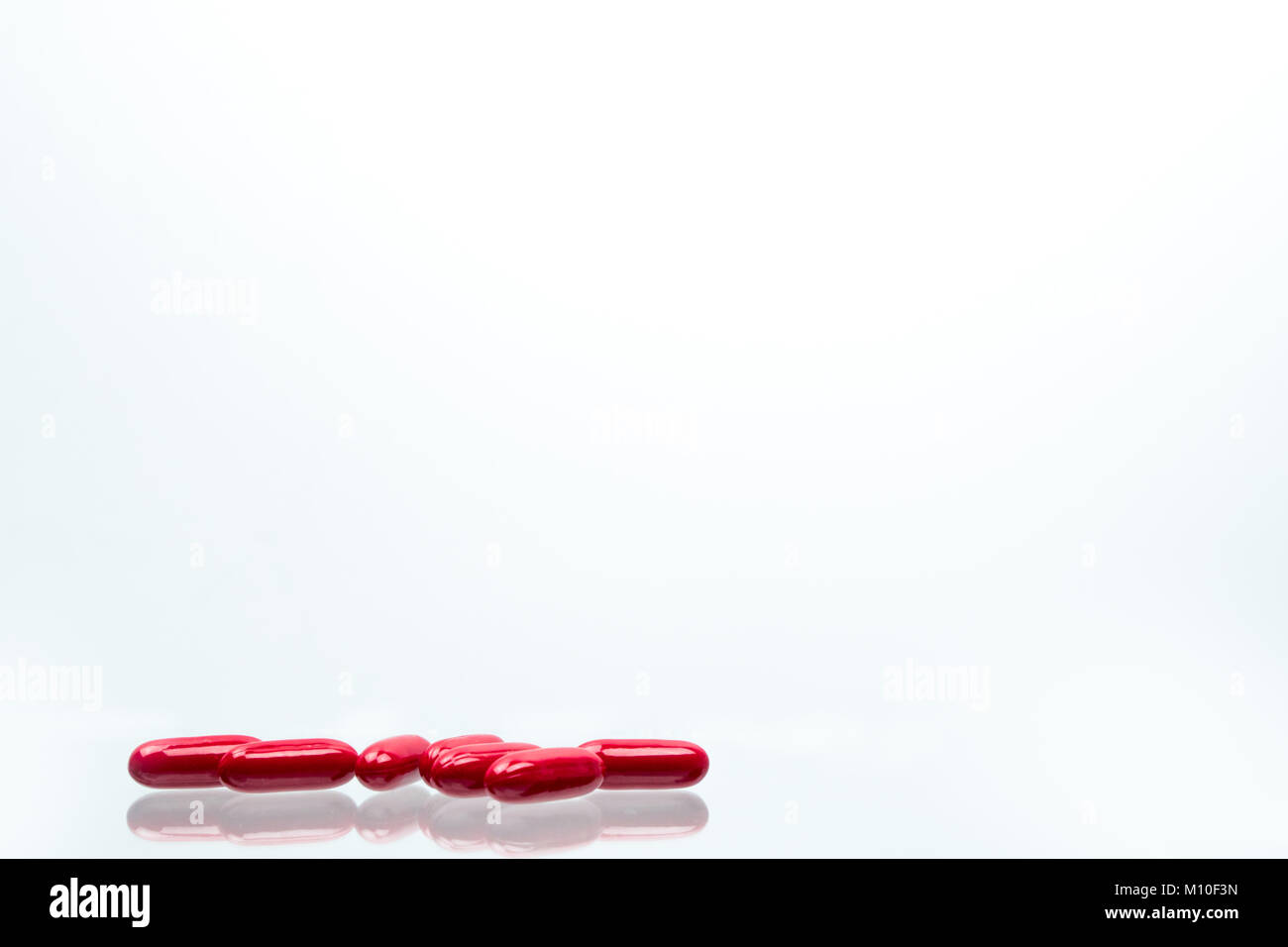 Red capsule pills isolated on white background with shadows and copy space for text. Vitamin and supplement for pregnancy and elderly people. Stock Photo