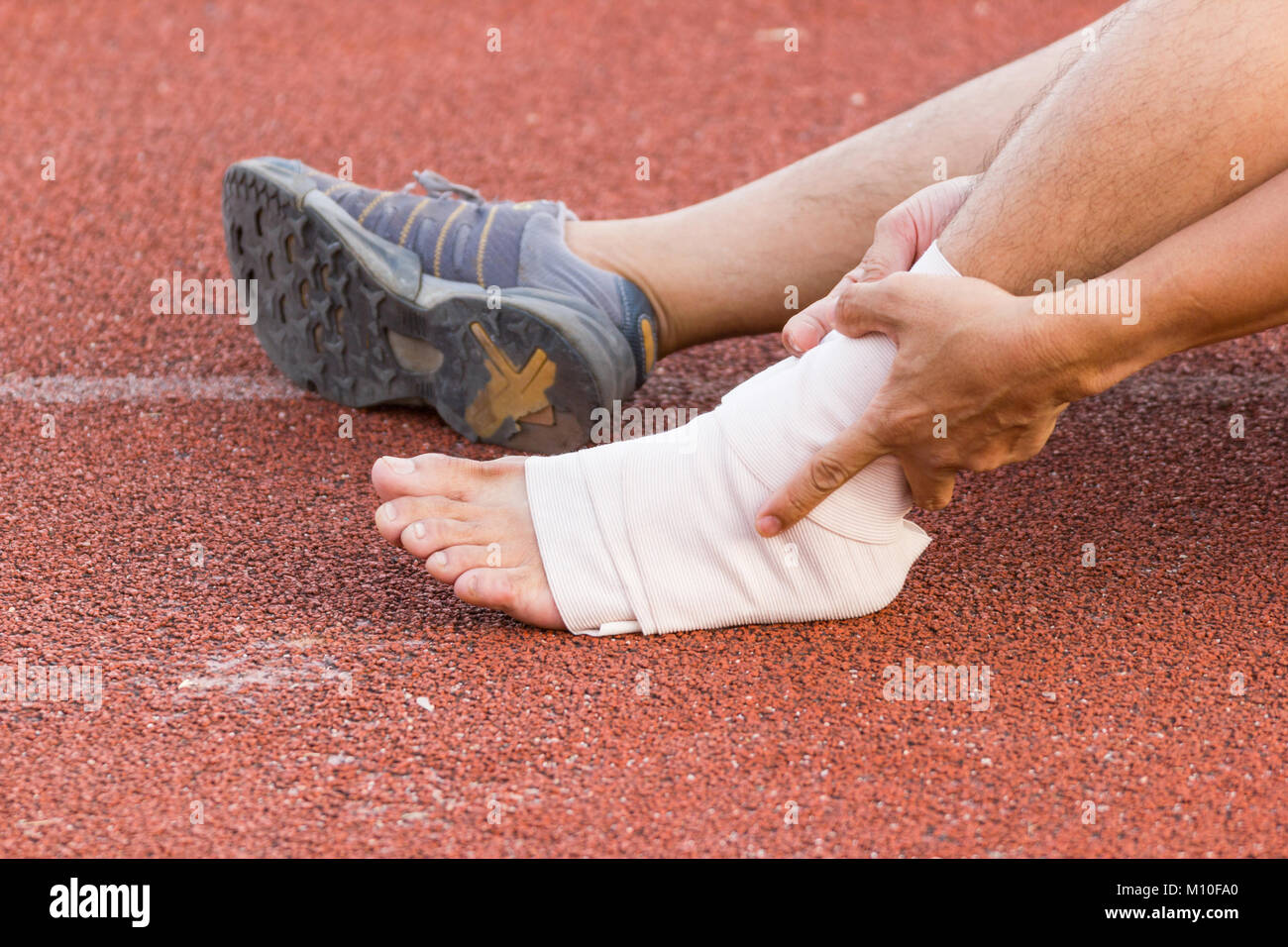 Male athlete applying compression bandage onto ankle injury of a