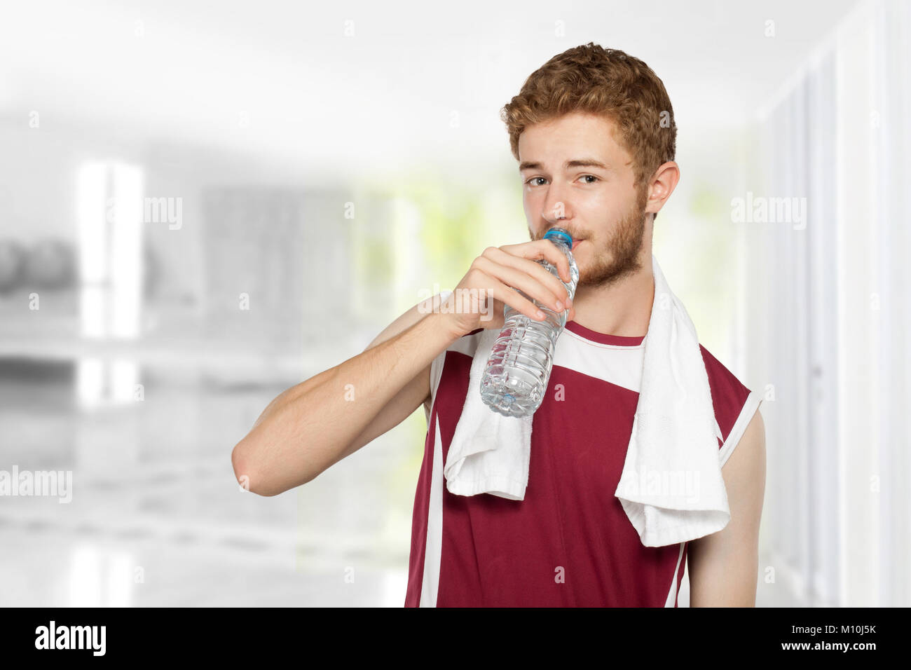 Portrait of healthy fitness man drinking a bottle of water in the gym ...