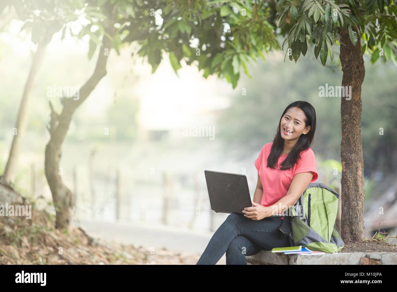A portrait of a young Asian student sitting outdoor, using a laptop ...